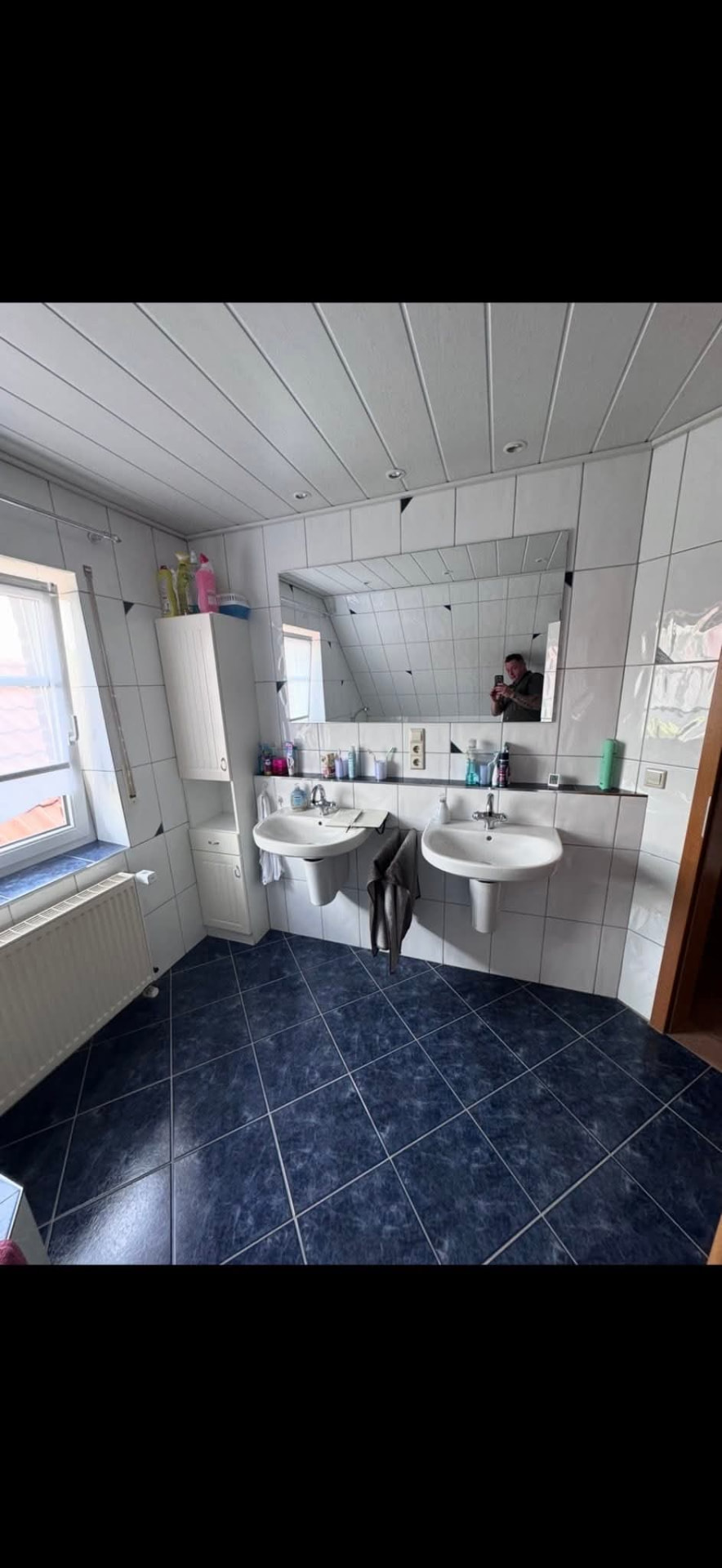 Altes Dachgeschossbad mit weißen Fliesen, dunkelblauem Fliesenboden und zwei Wandwaschbecken